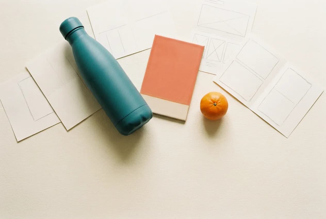 Teal bottle with blank layout studies and color swatches on an ivory creative desk